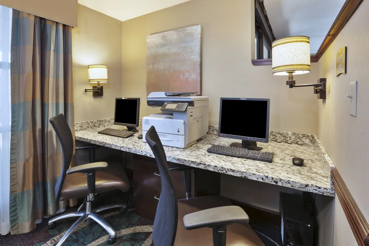 This image displays a dedicated business center featuring granite countertops, computers, and a printer. The scene is designed for focused work, with a clean and professional layout ideal for business travelers.