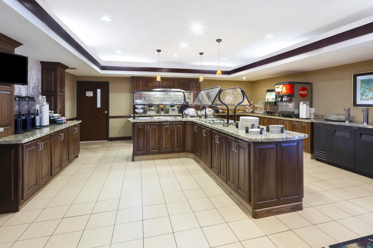 A bright buffet counter set with a coffee station and drink dispenser, designed for guests to enjoy a complimentary breakfast. The area has a friendly, welcoming ambiance ideal for morning routines and social interaction.