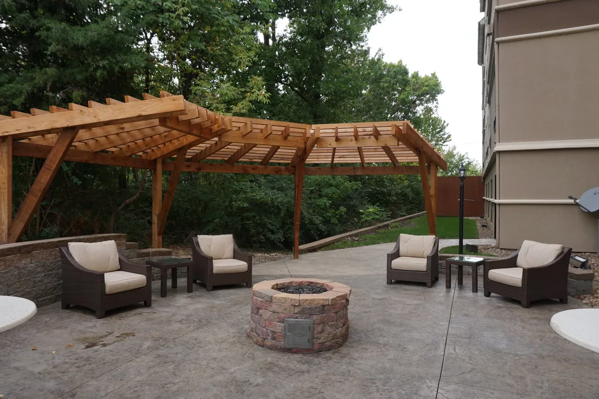 A cozy exterior lounge area under a wooden pergola, centered around a fire pit with comfortable seating. The space is designed for socializing and relaxing outdoors in the evening or early morning, perfect for families winding down after a day of adventure.