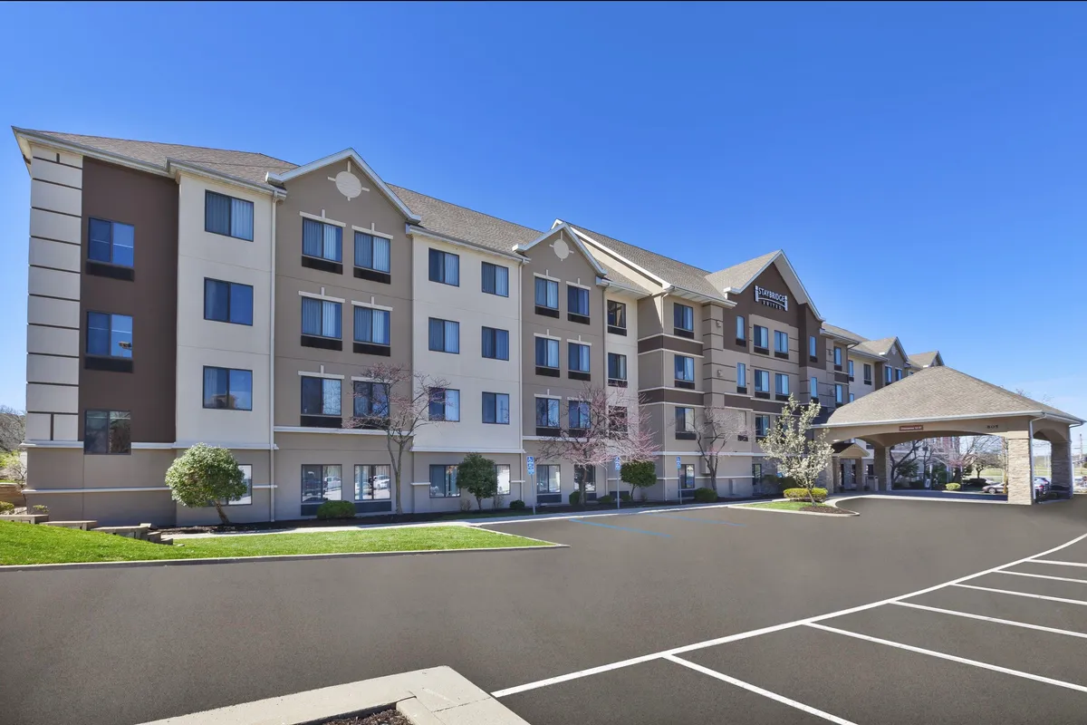 This inviting exterior image showcases the hotel entrance surrounded by landscaping, with large windows and a glimpse of the parking lot. It visually represents the property's accessibility and proximity to local attractions, such as the university and downtown district.