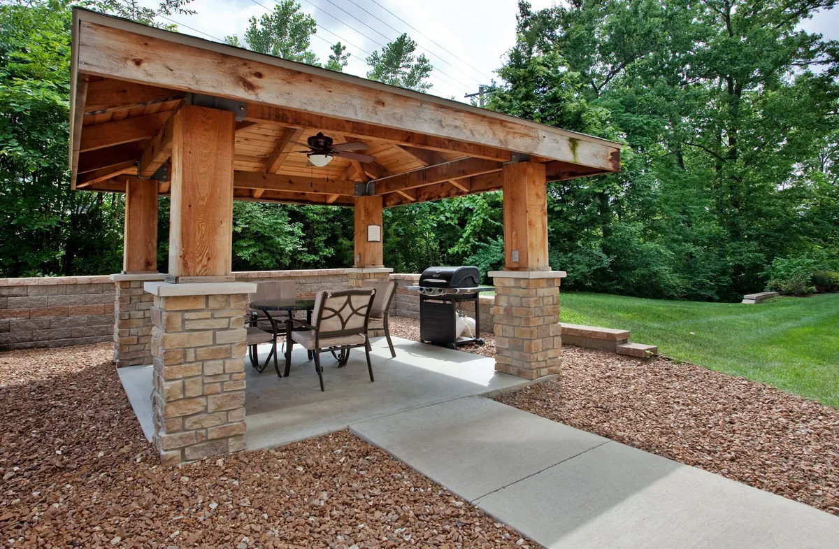 An inviting scene featuring a wooden gazebo, grill, dining table, and lush greenery, ideal for outdoor dining or casual gatherings. The area encourages interaction and celebration, perfect for families, alumni, and groups visiting the university or downtown district.